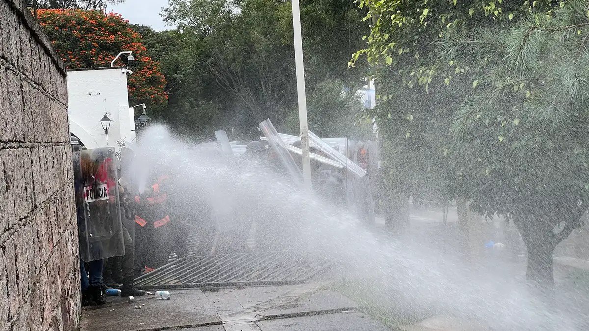 Policías antimotines lanzan chorros de agua a presión contra manifestantes frente a Casa Jalisco durante la marcha por agua limpia en Guadalajara