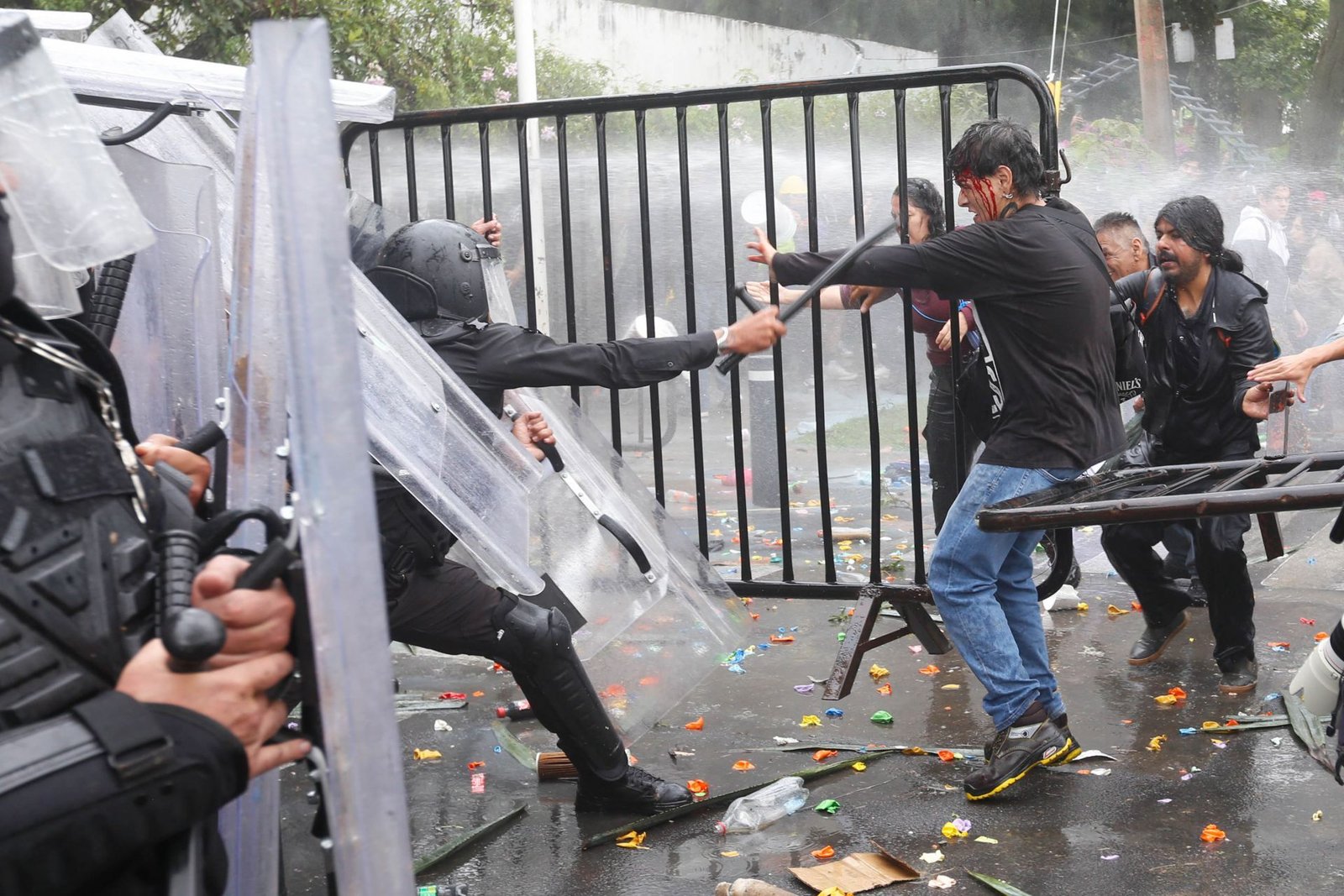 Un policía antimotines con bastón y un manifestante herido junto a una valla durante la represión de la marcha por agua limpia en Casa Jalisco, Guadalajara